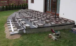 Budowa tarasu kompozytowego: betonowe bloczki podtrzymują legary, tworząc solidną podstawę.