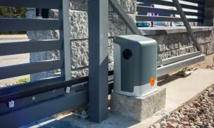 Nowoczesny mechanizm bramy przesuwnej z napędem Nice, zamontowany przy kamiennym słupku i metalowej konstrukcji bramy.