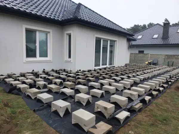 Budowa tarasu z deski kompozytowej na bloczkach betonowych. Podkład z agrowłókniny chroni przed chwastami.