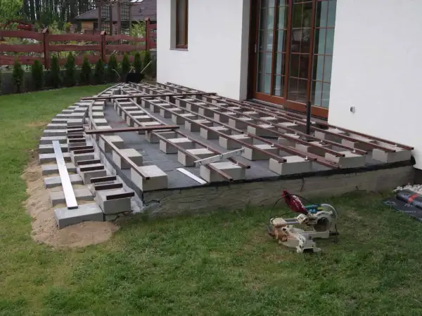 Budowa tarasu kompozytowego: betonowe bloczki podtrzymują legary, tworząc solidną podstawę.